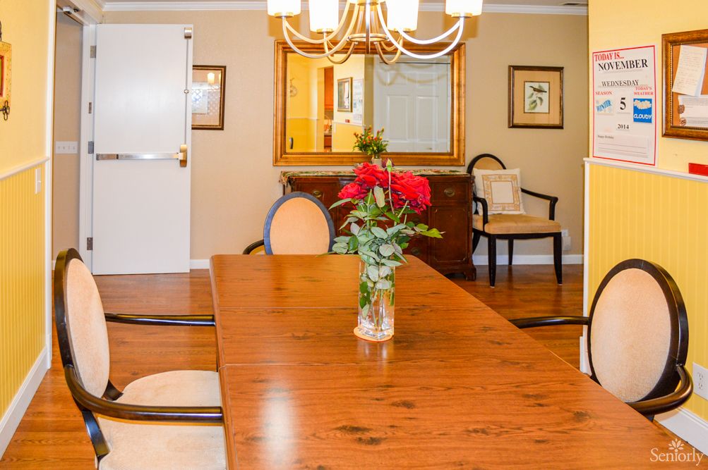 A cozy dining room featuring a wooden table with chairs, a chandelier, and a vase of flowers as a centerpiece.