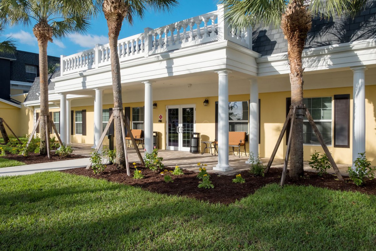 A sunny view of a house with a patio, surrounded by palm trees and a well-manicured lawn.