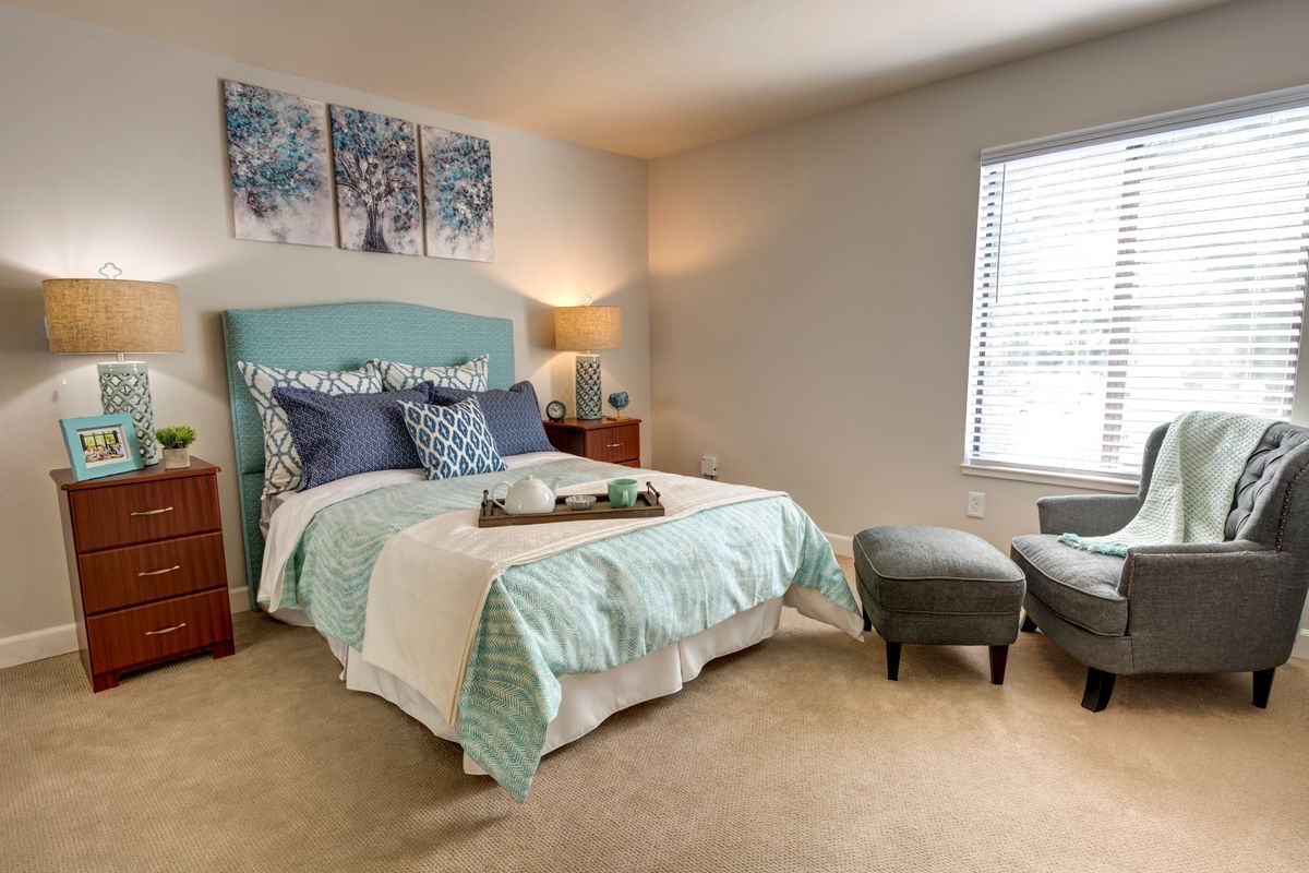 A cozy bedroom with a neatly made bed, soft lighting, and wall artwork.