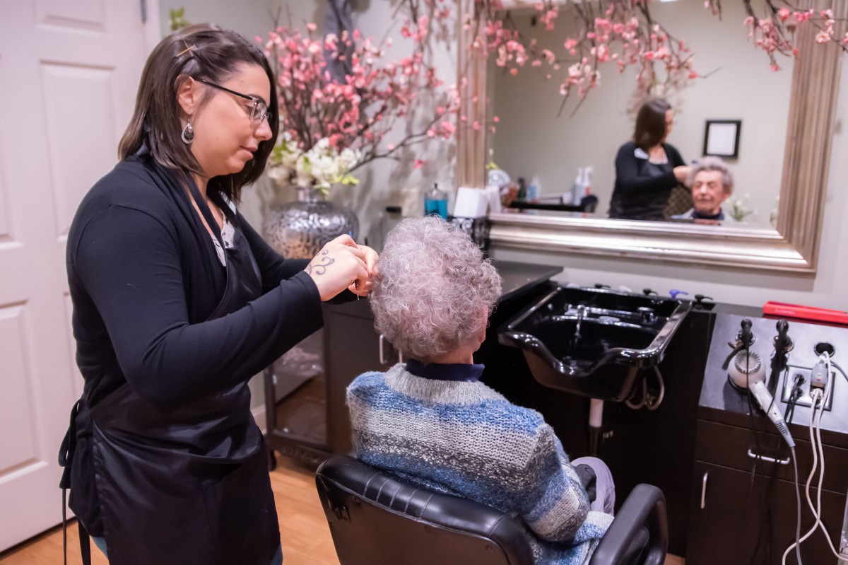 A hairdresser styles an elderly woman's hair in a salon setting.