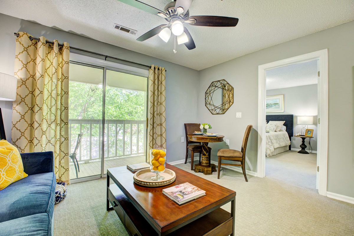 A modern living room with a coffee table and chairs, featuring a ceiling fan and balcony view.