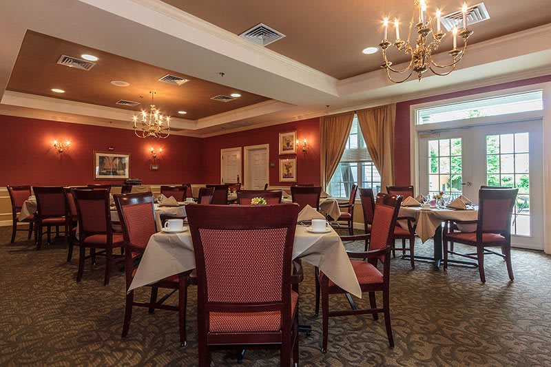 An elegantly decorated dining room with neatly arranged tables and chairs, adorned with chandeliers and curtains.