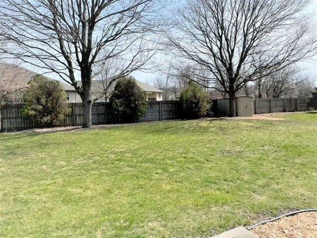 A grassy yard with trees and a fence on a clear day.