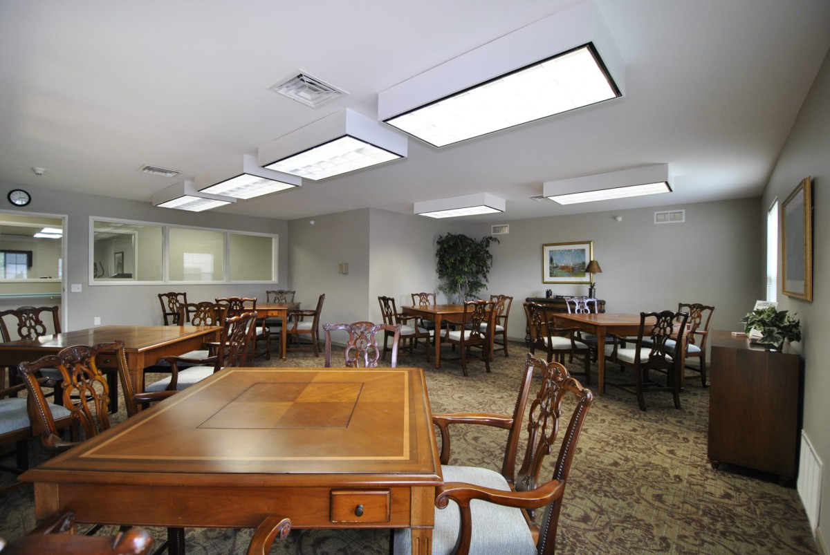 A well-lit meeting room with multiple wooden tables and chairs, suitable for gatherings or conferences.