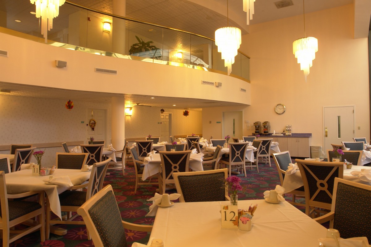 A modern restaurant dining area with empty tables set for service beneath elegant chandeliers.