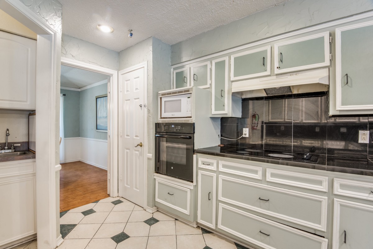 A modern kitchen with white cabinets, featuring a built-in oven and microwave.