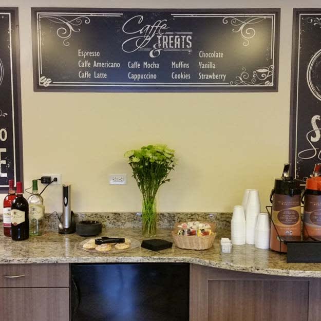 A coffee station with a menu board above, cups, and a vase of flowers on the counter.