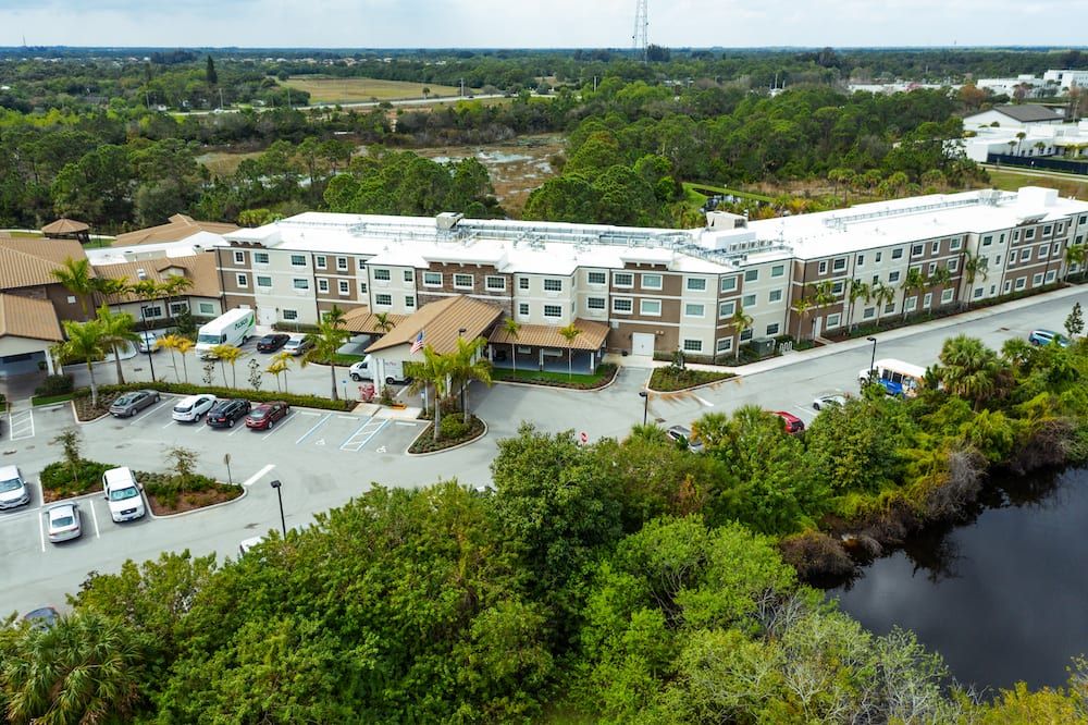 Aerial view of a hotel surrounded by trees with a parking lot in front.