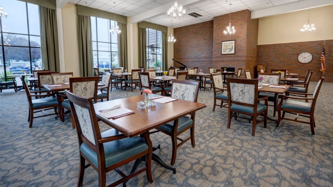 An elegant dining room with neatly arranged tables and chairs, featuring large windows and stylish lighting.
