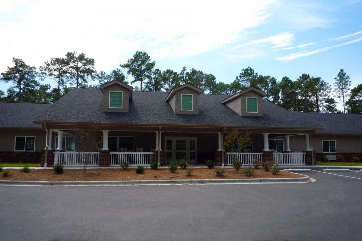 A residential house with a porch and dormer windows, surrounded by trees.