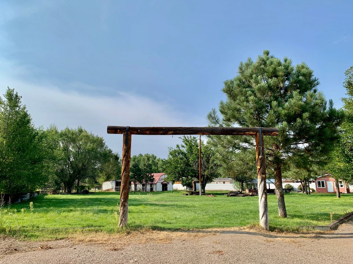 A serene landscape with a wooden frame, lush green grass, and trees against a clear blue sky.
