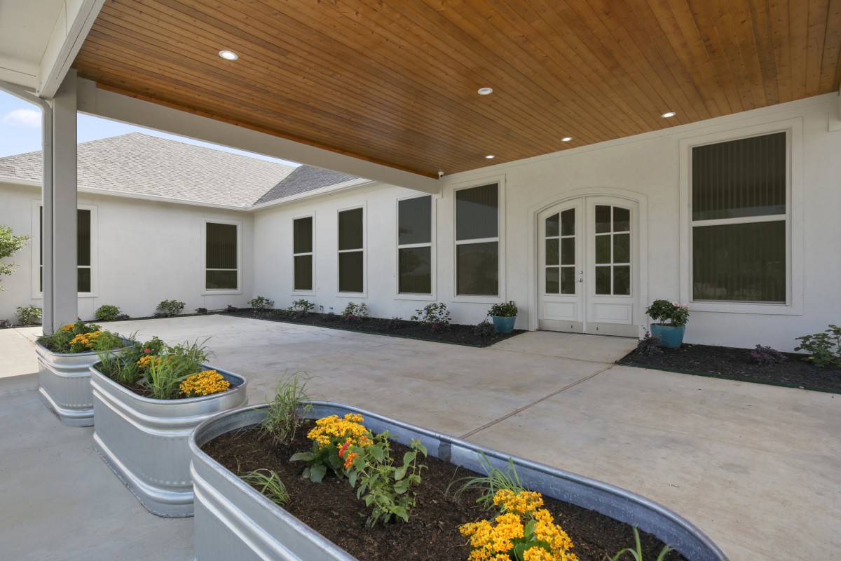 A modern building entrance featuring a wooden ceiling, large windows, and decorative planters with vibrant flowers.