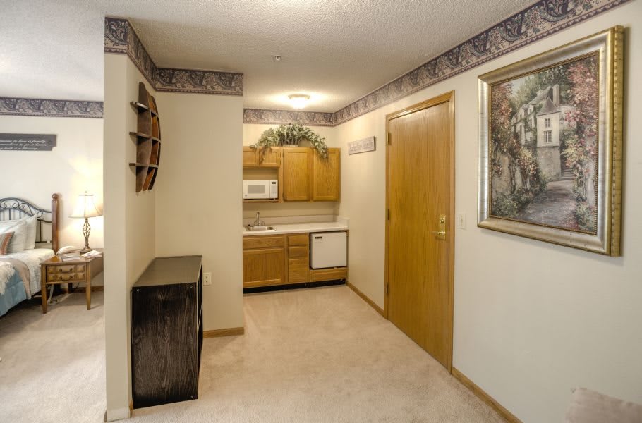 A small apartment hallway leading to a kitchen area with wooden cabinets and carpet flooring.