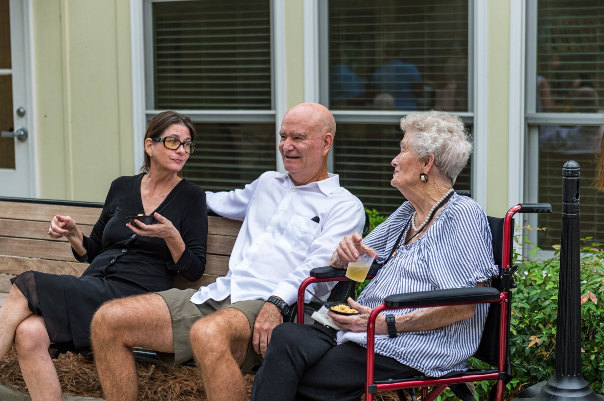 A group of three people engaged in a conversation outside on a patio.