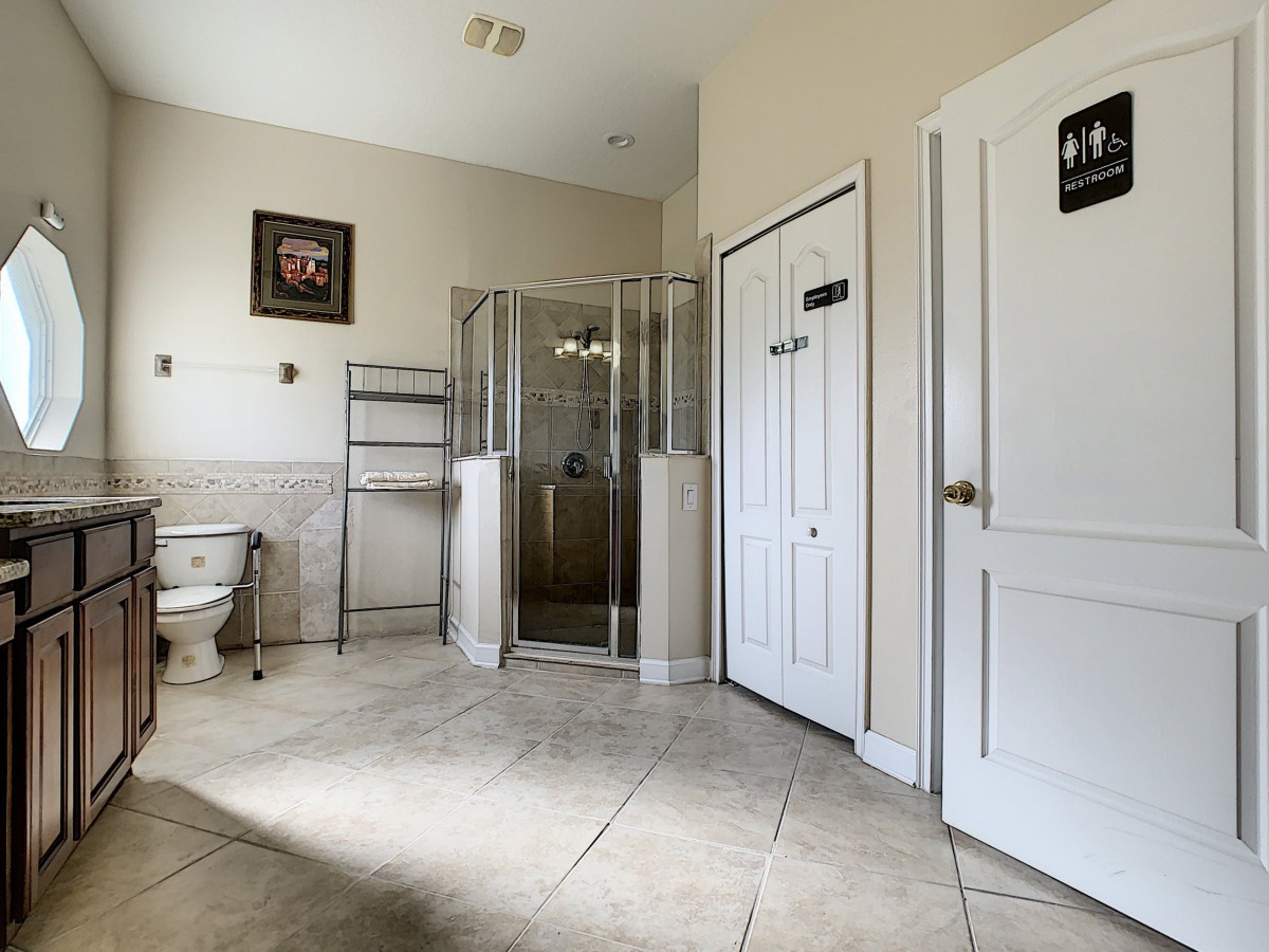 A spacious bathroom featuring a glass-enclosed shower, a toilet, and tiled flooring.