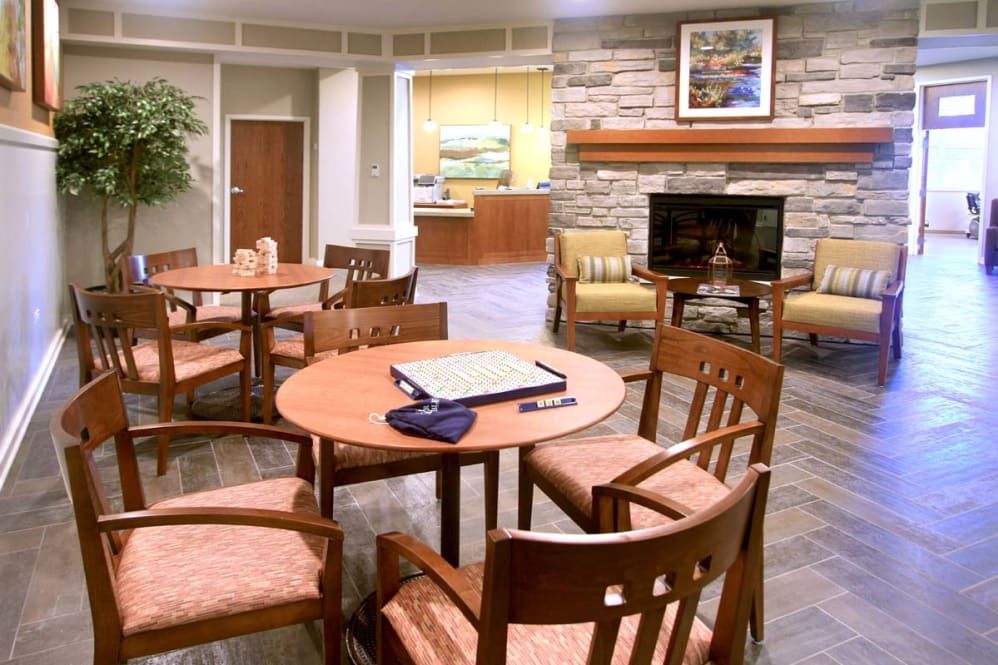 A cozy lounge with wooden tables and chairs, featuring a television and a fireplace in the background.