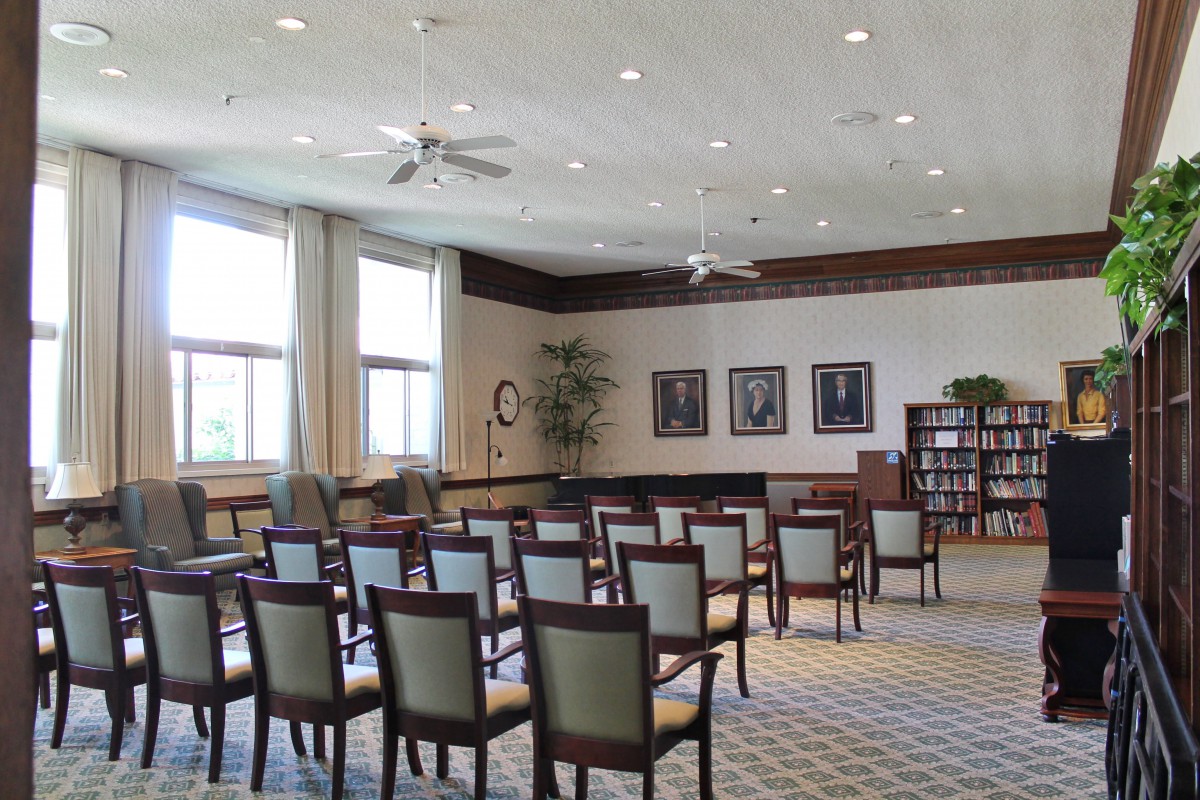 An empty conference room with arranged chairs and bookshelves, illuminated by natural light from large windows.