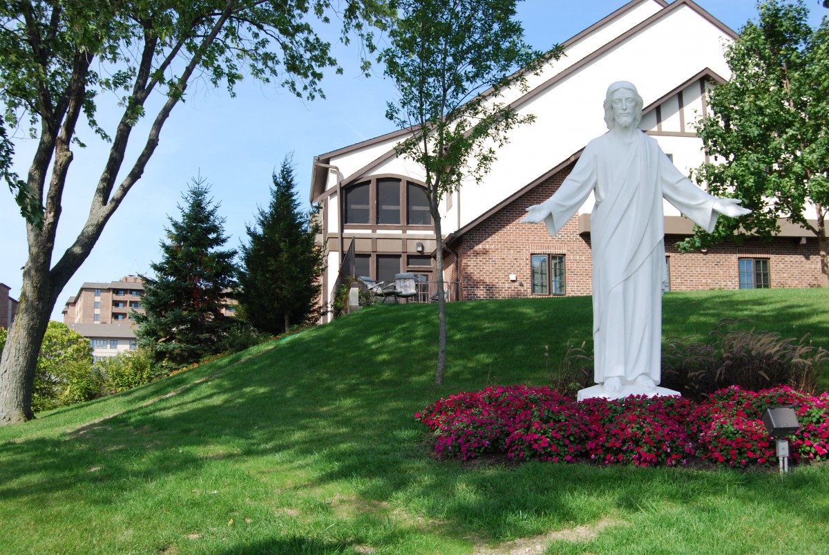 A statue stands in front of a building surrounded by trees and manicured landscaping.