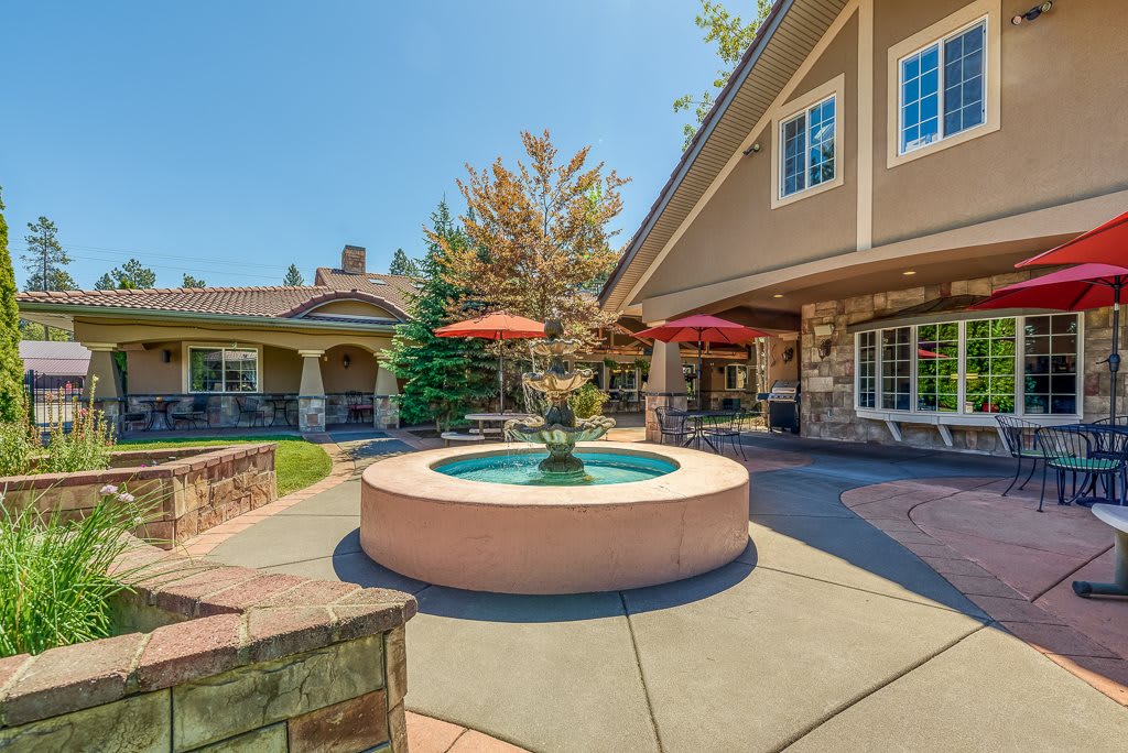 A scenic outdoor area featuring a fountain, surrounded by a patio with umbrellas and landscaping.