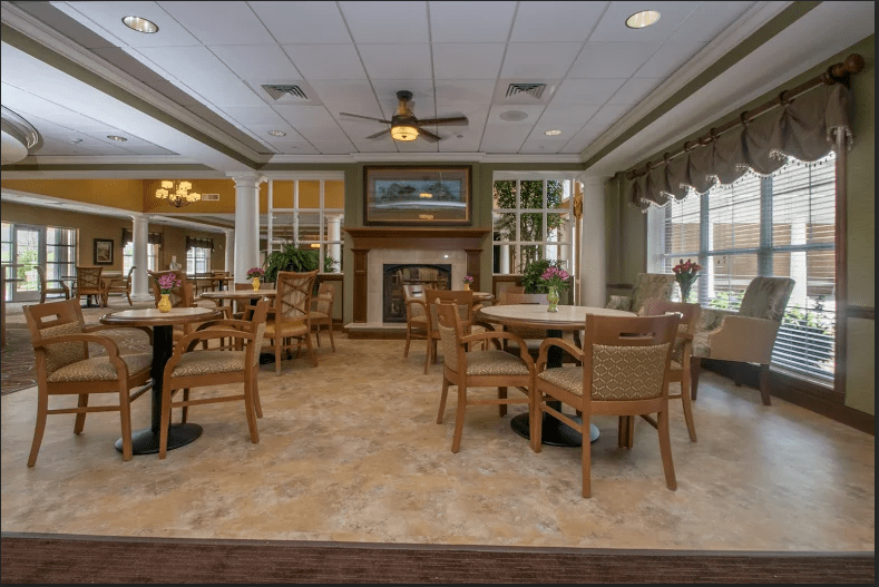 A cozy dining area with tables and chairs, featuring a central fireplace and ample natural light.