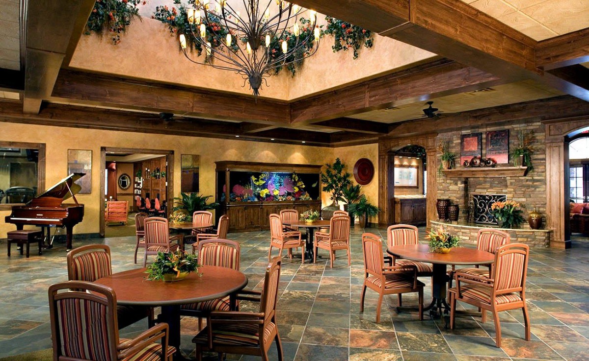 A cozy interior lounge with tables and chairs, decorated with plants and a chandelier.