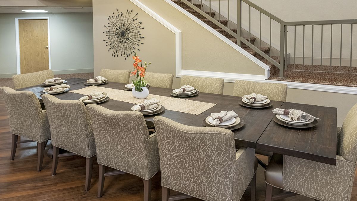 Elegant dining room with a large table set for eight, featuring modern decor and a decorative wall piece.