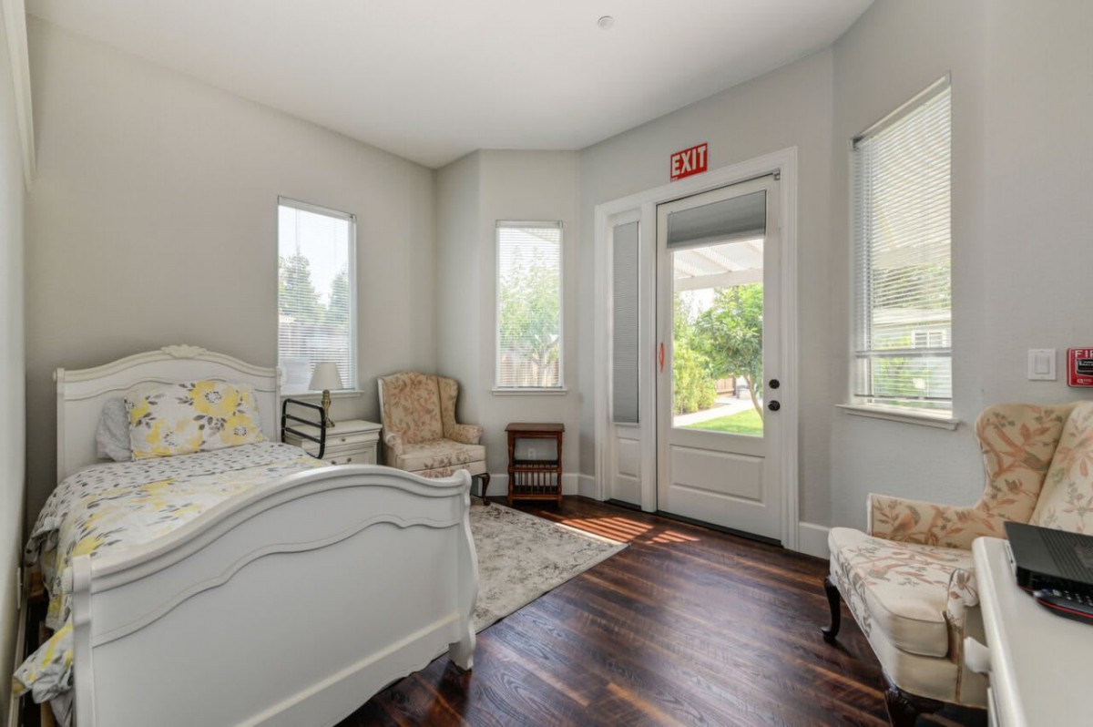 A cozy bedroom with natural light, featuring a bed, chair, and hardwood flooring.