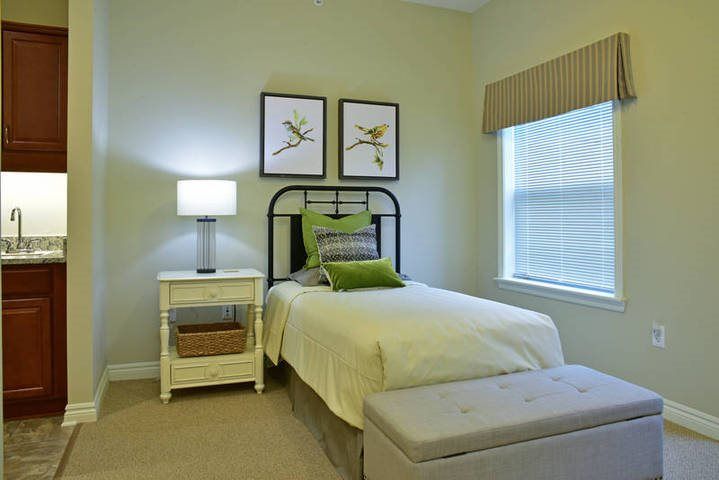 A minimalist bedroom featuring a single bed with green accents, a nightstand with a lamp, and framed artwork on the wall.