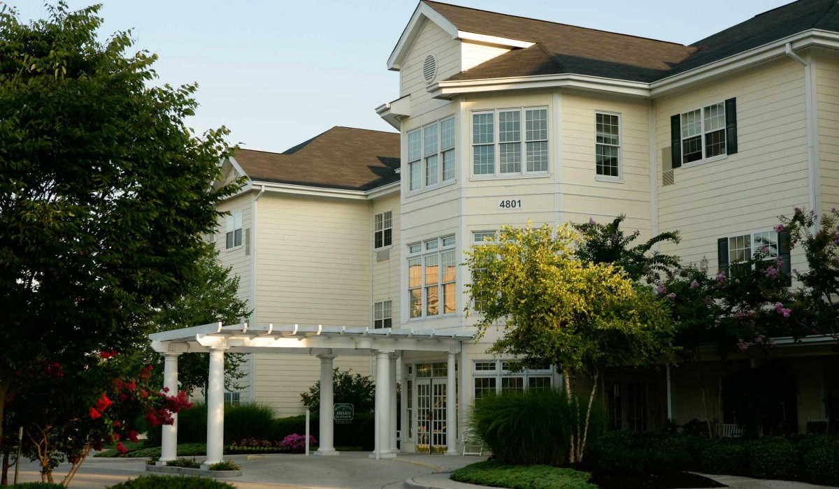 A large residential building with multiple windows and a white exterior, surrounded by trees.