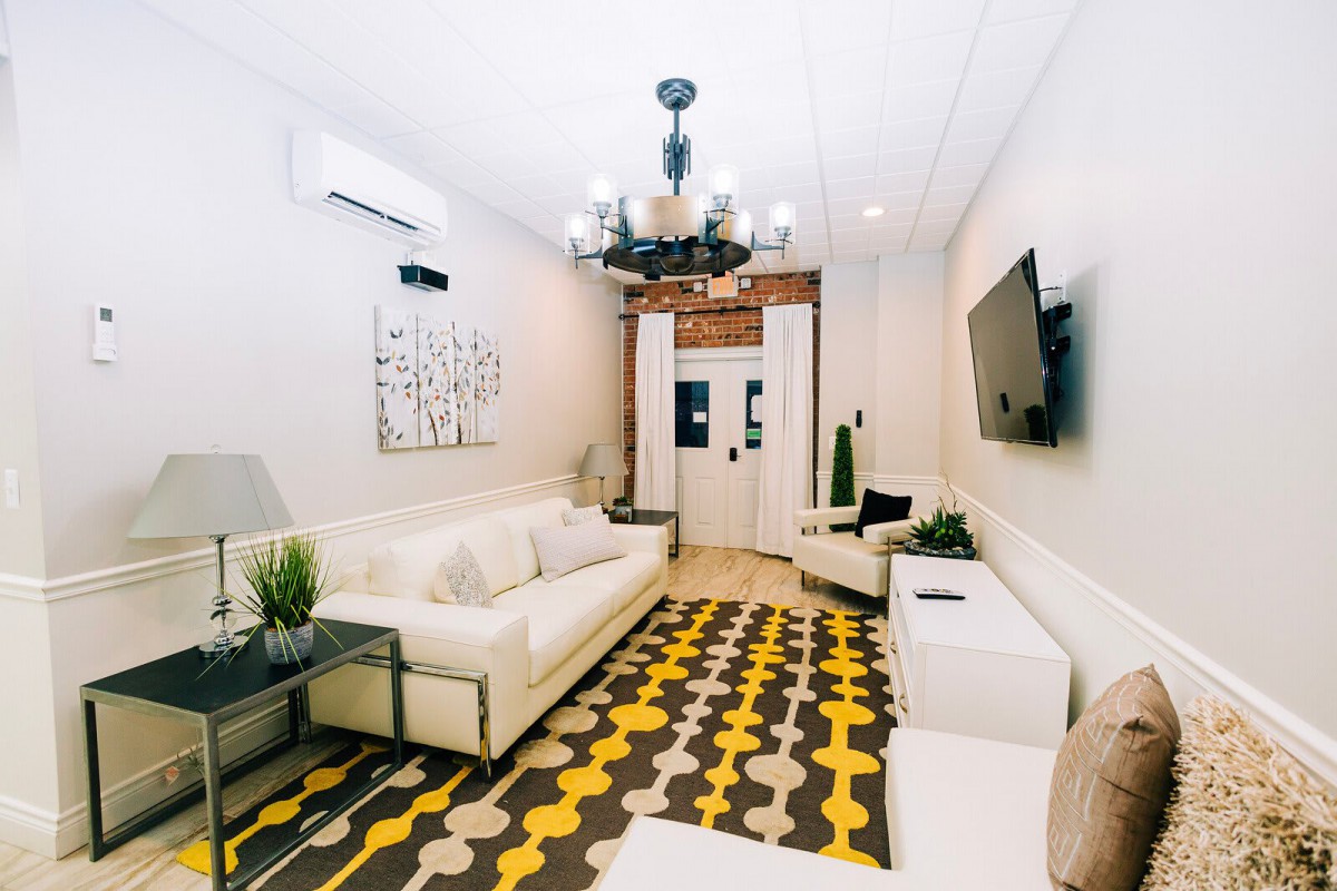 A modern living room featuring a white sofa, decorative rug, and chandelier.