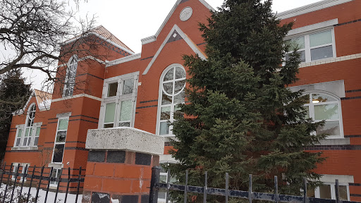 A beautifully designed red brick building partially covered in snow, framed by a lush evergreen tree.