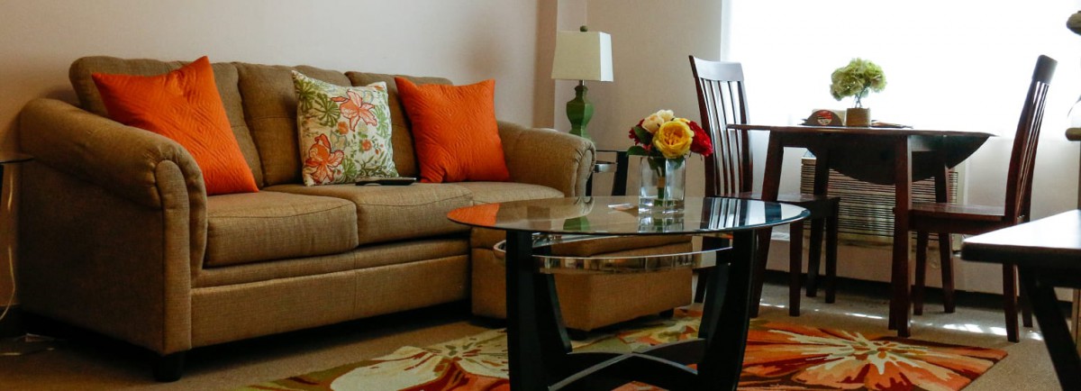 A cozy living room with a sofa adorned with colorful cushions, a glass coffee table, and a decorative lamp.
