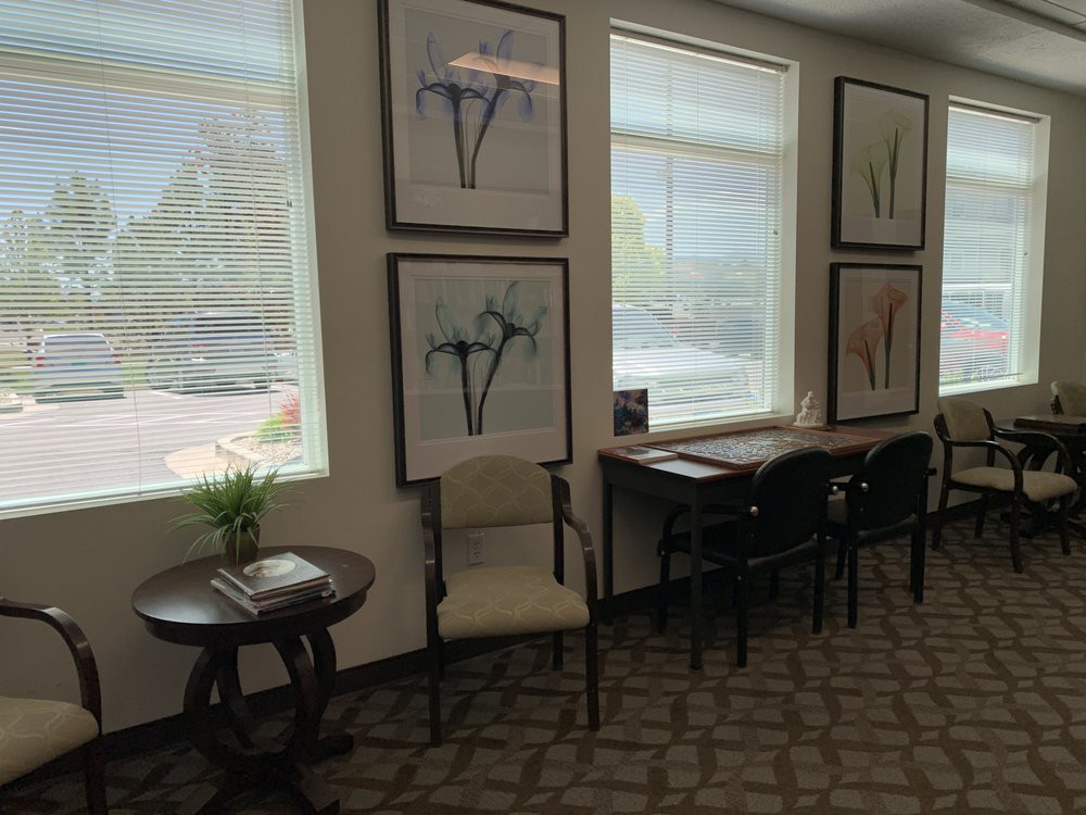 A waiting room with artwork on the walls, chairs, and tables by the window.