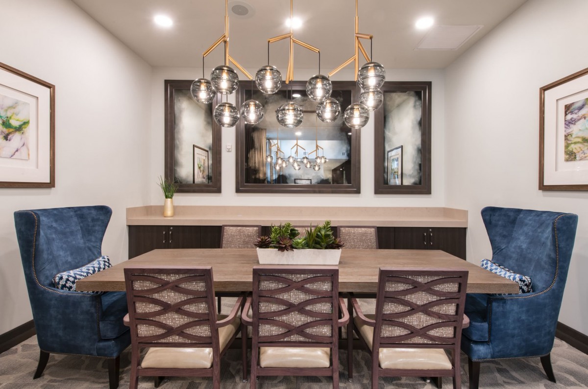 A modern dining room featuring a stylish chandelier, a wooden table with six chairs, and decorative plants.