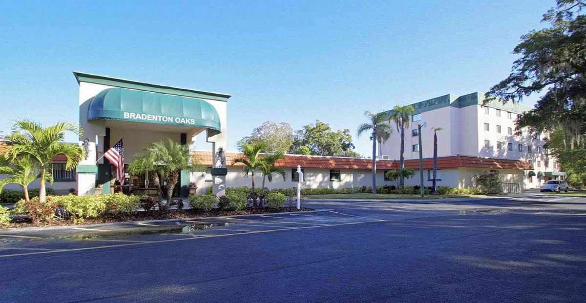 A hotel with a parking lot and palm trees on a sunny day.
