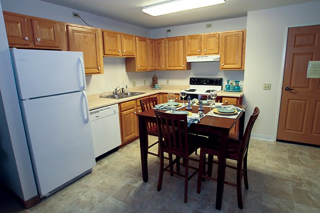 A cozy kitchen with wooden cabinets, a dining table set for four, and modern appliances including a refrigerator, stove, and dishwasher.