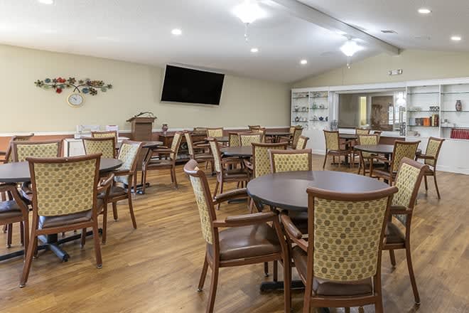 A spacious dining area with several tables and chairs, featuring a wall-mounted television.
