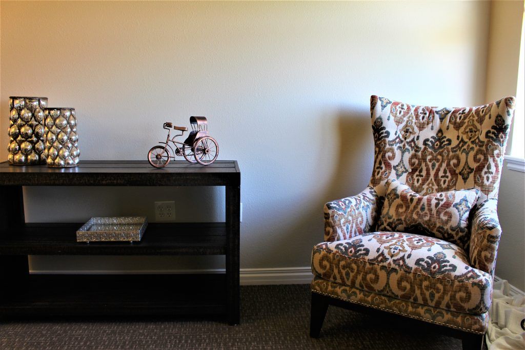 A stylish living room corner featuring a patterned armchair and a shelf with decorative items.