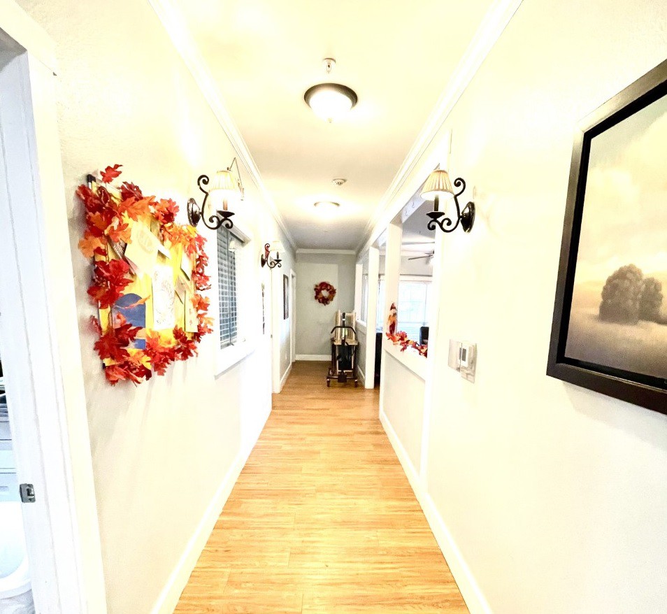 A brightly lit hallway with wooden flooring and decorative wreaths on the walls.