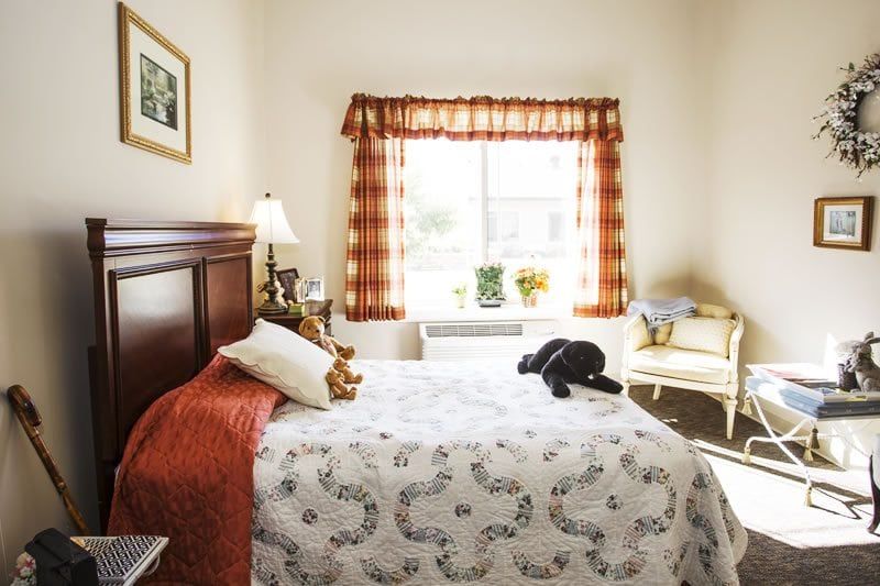 A cozy bedroom with natural light coming through a window, featuring a neatly made bed and warm decor.