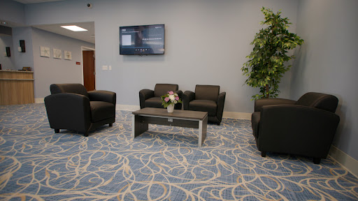 A modern waiting area featuring comfortable black chairs, a coffee table, and a television.