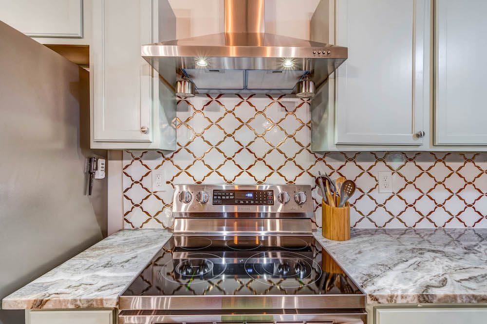 Modern kitchen with a stylish stove, intricate backsplash, and sleek range hood.