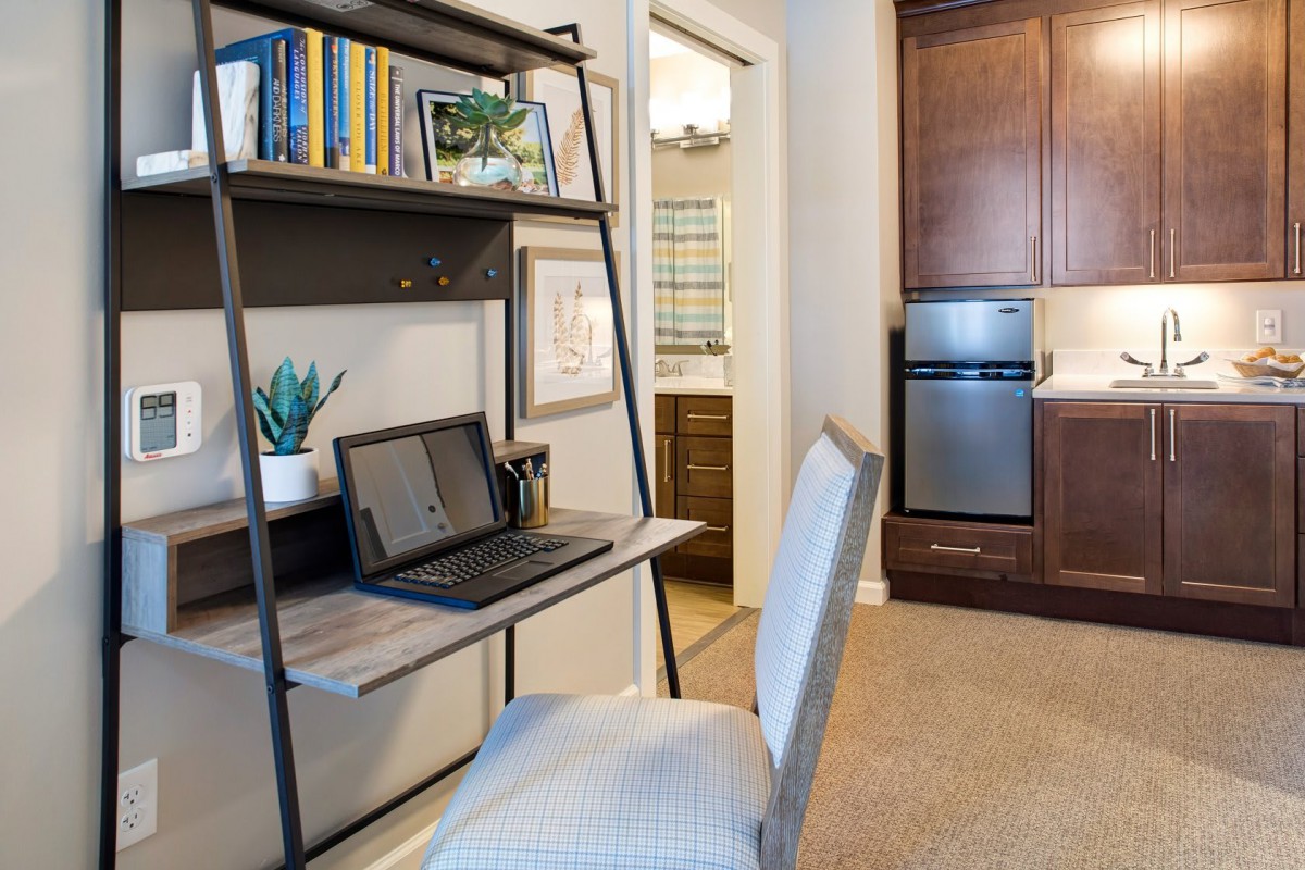 A compact home office setup in an apartment, featuring a desk with a laptop, bookshelf, and a comfortable chair.