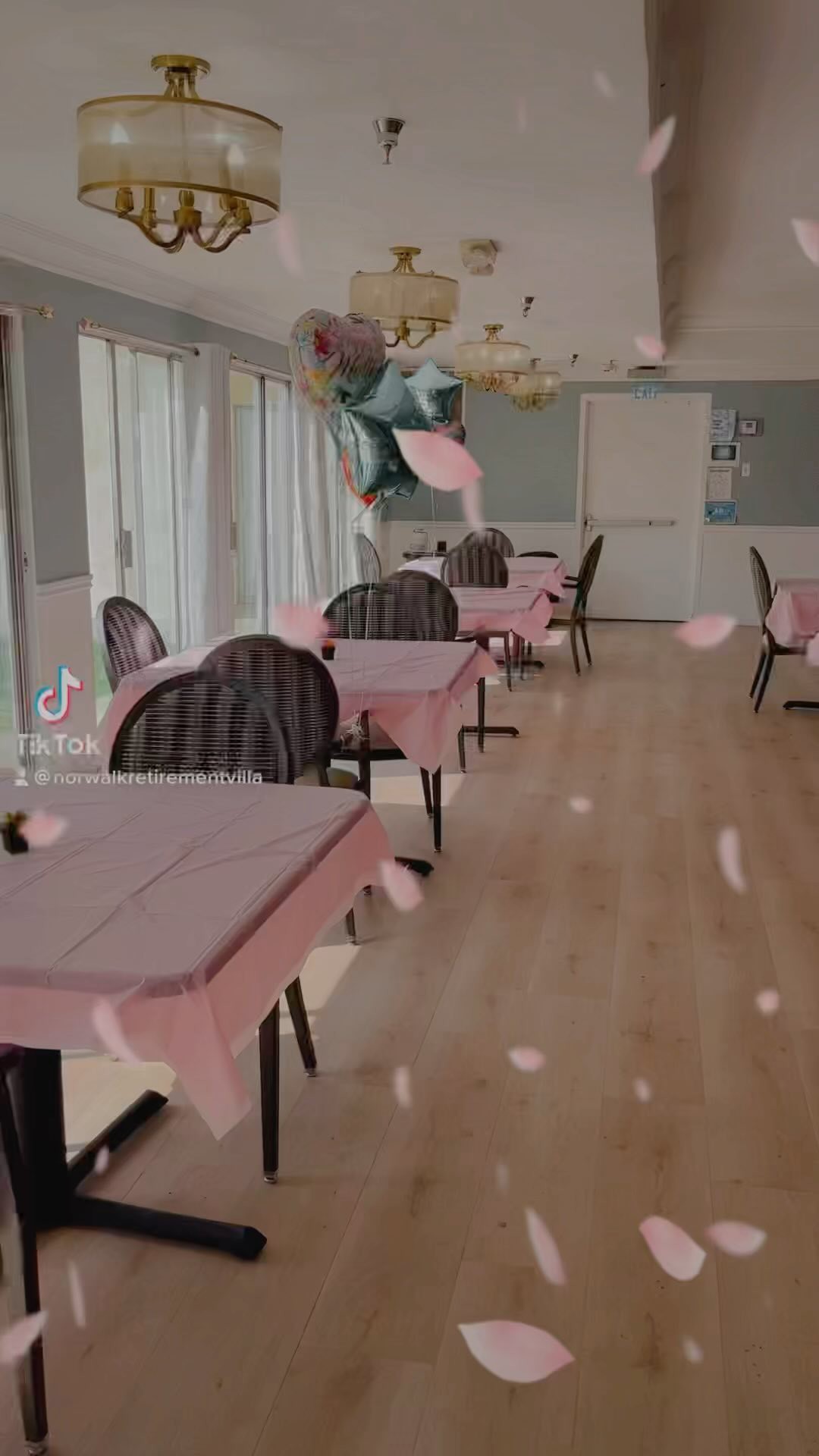 An empty dining room decorated with balloons and pink tablecloths.