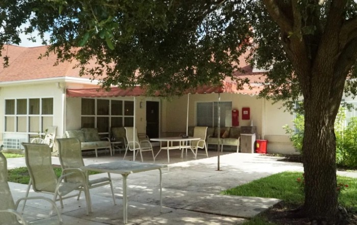 A peaceful outdoor patio area with tables and chairs under the shade of a large tree.