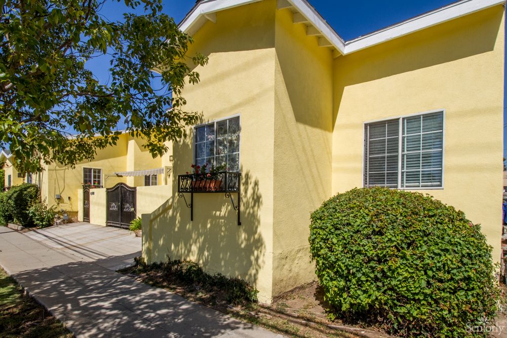 A bright yellow residential building with windows and surrounding greenery on a sunny day.