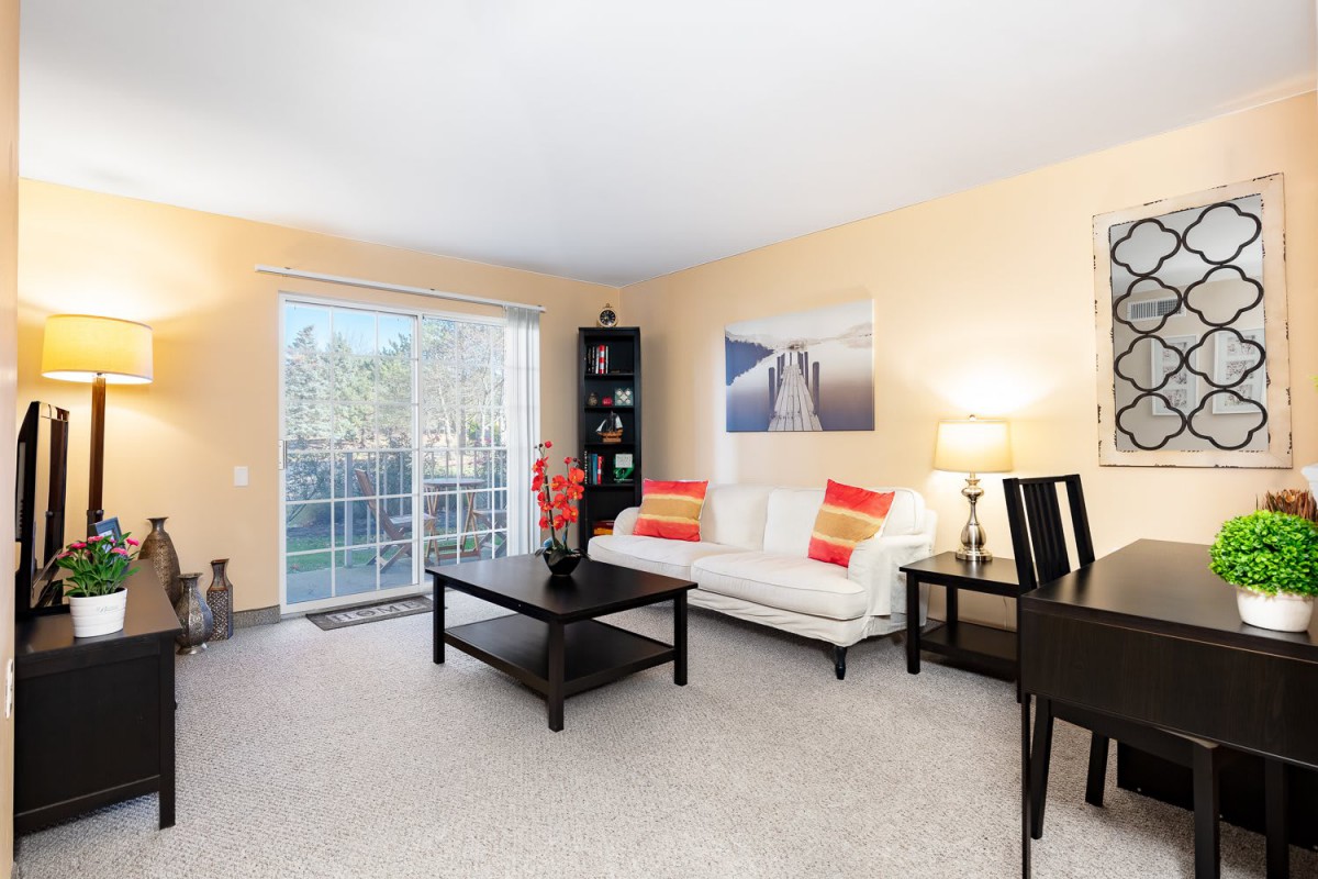 A modern living room with a white sofa, colorful pillows, and a coffee table, featuring a sliding glass door that lets in natural light.