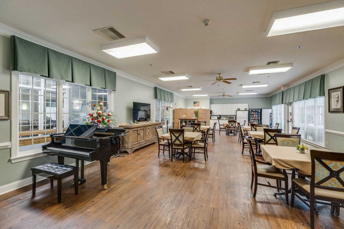 A spacious interior with a piano, dining tables, and chairs on a hardwood floor.