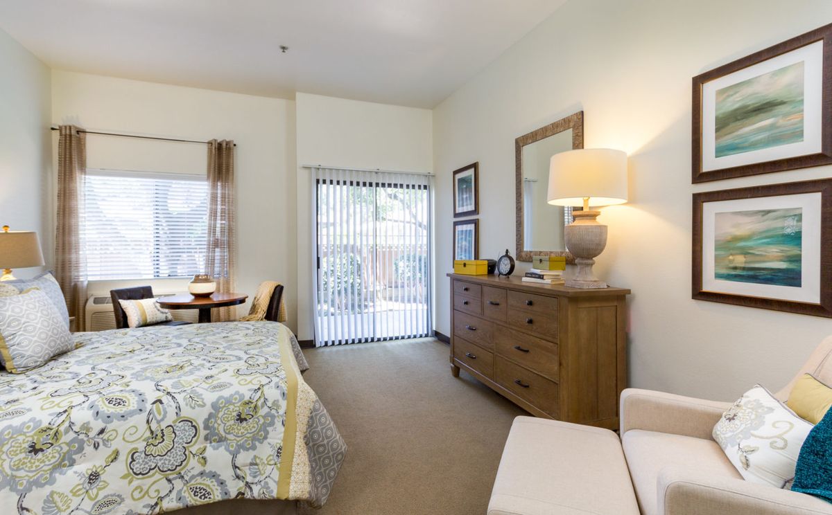 A cozy bedroom with a neatly arranged bed, dresser, and mirror, featuring warm lighting and soft decor.
