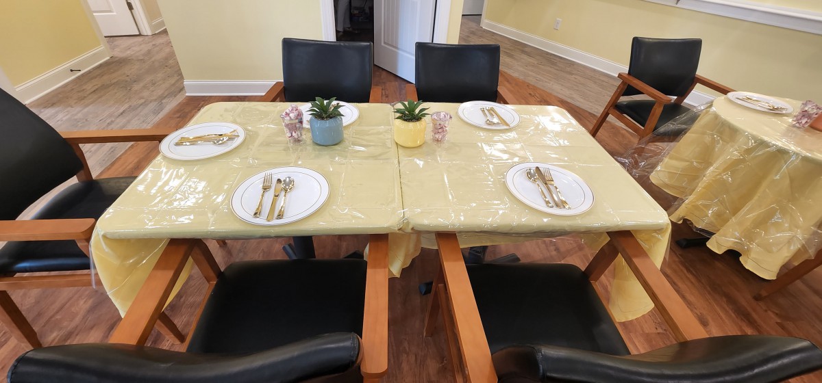 A dining table set for four with plates, cutlery, and decorative plants.